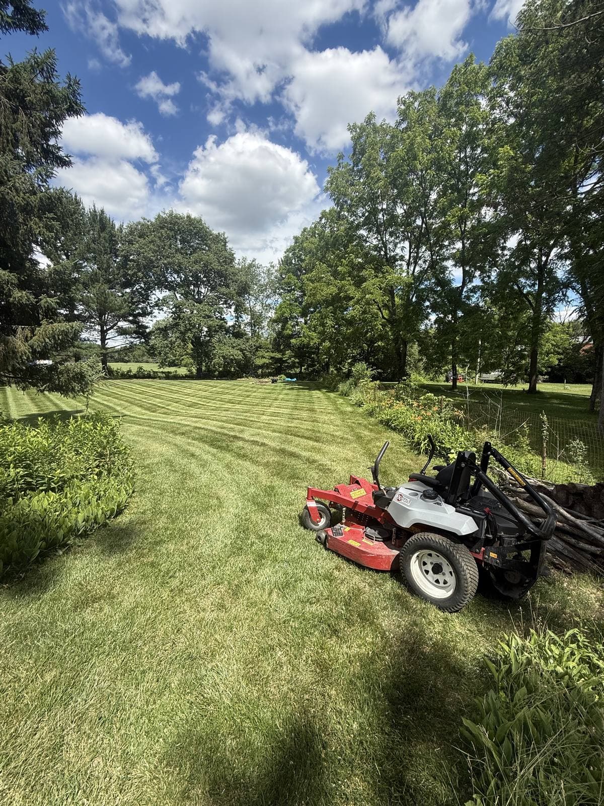 A red zero-turn mower on a freshly striped lawn under a bright blue summer sky