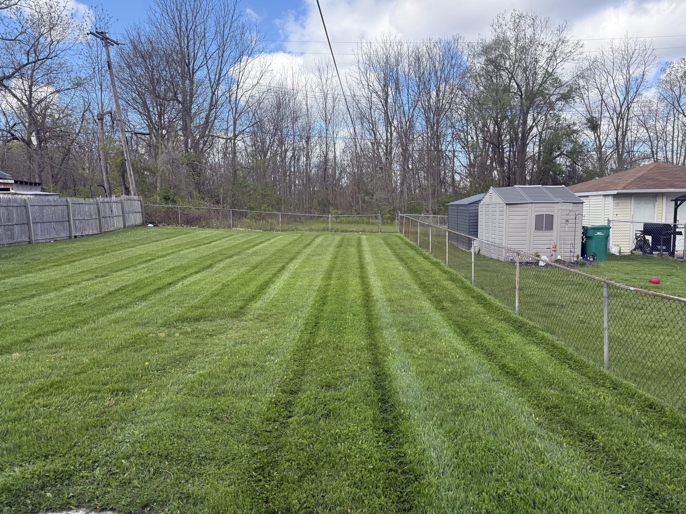 A fenced backyard mowed in crisp green stripes