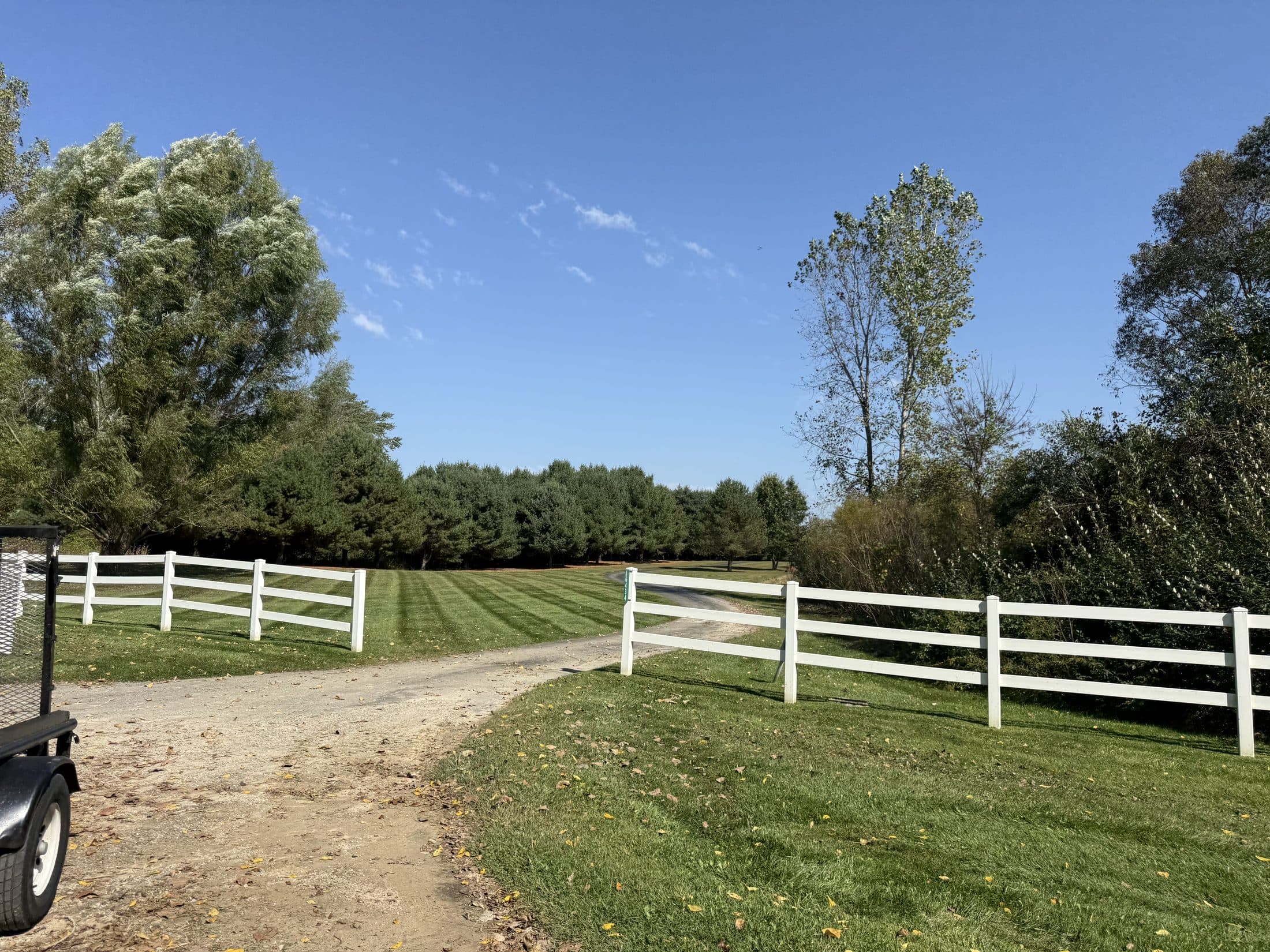 A rural property with a white rail fence and freshly cut grass